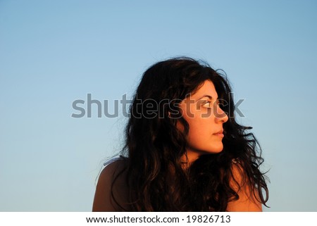 A beautiful mediterranean woman in profile against a clear sky background.