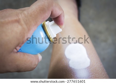 spraying suntan lotion on legs