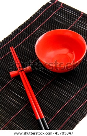 Red bowl and chopsticks resting on chopstick rests (against a black bamboo background)