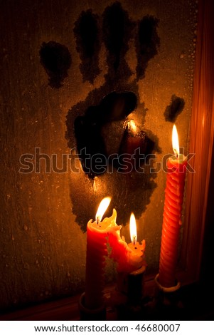Horror (three candles burning in the darkness and lighting a frozen window with a black handprint)