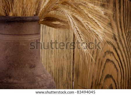 Old crock with a bunch of wheat ears (against the background of a wooden wall, with focus on wheat ears), retro style