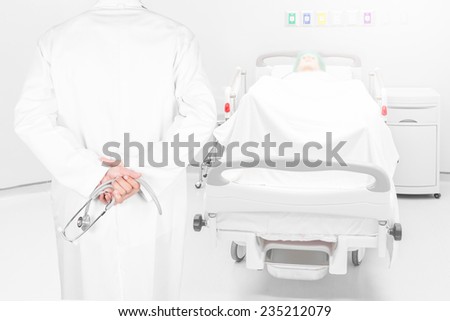 Close-up rear view image of doctors with stethoscope pose arms crossed behind back looking at pateint bed in hospital room