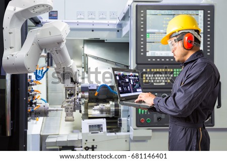 Maintenance engineer using laptop computer control automatic robotic hand with CNC machine in smart factory. Industry 4.0 concept