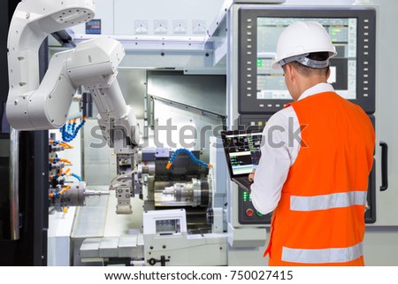 Engineer using laptop computer for maintenance automatic robotic arm with CNC machine in smart factory. Industry 4.0 concept