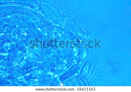 Circles waves are dispersing on transparent blue water.