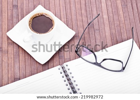 Cup of coffee with glasses and notebook on a wooden background made of bamboo