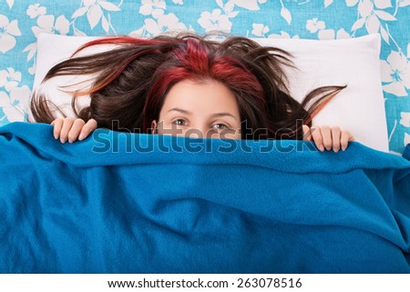 Good morning you... Young girl hiding behind her face behind a blanket in her bed