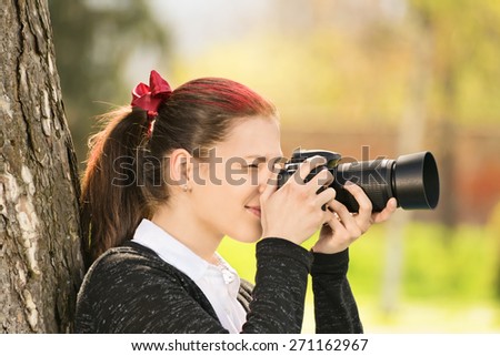 Taking photographs outdoor. Young girl shooting her camera.