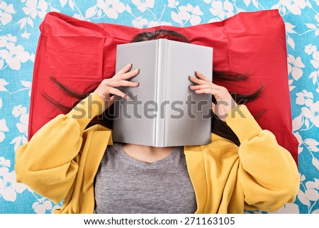 Ah, this read never seems to end. Young girl in her bed covering her face with an open book, as if she\'s really tired/bored of reading