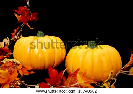 Two bright orange pumpkins arranged against a black background with some fall leaves to the left.
