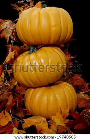 Three orange autumn pumpkins stacked ontop of each other on a black background with some leaves.