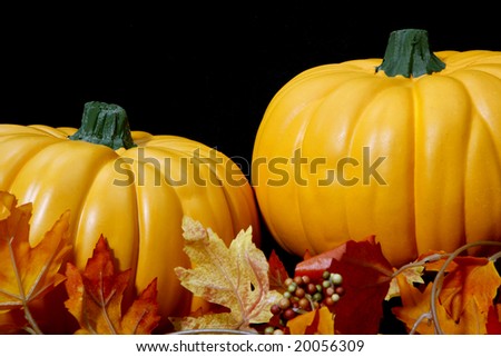 Two orange autumn pumpkins arranged on a black background with some leaves.