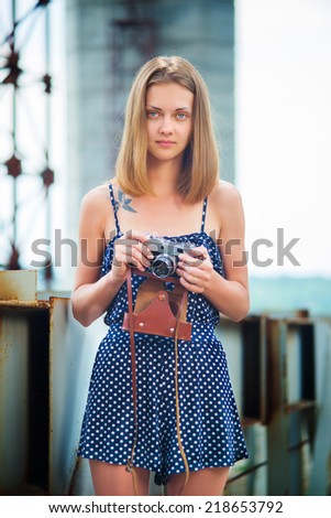 Young slim woman in a blue sundress standing on the line and keep the old vintage camera in the hands of
