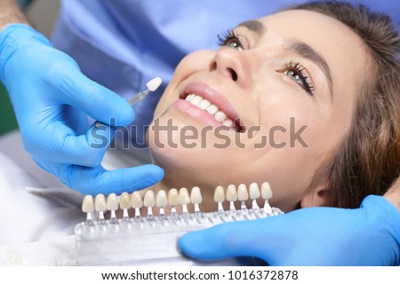 In a professional practice, a dentist checks the level of teeth whitening the patient\'s teeth with a dentist\'s color. Concept of: dentists, healthcare, perfection, white.