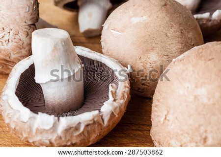 Closeup on three champignon mushrooms on wooden cutting board two faced with caps and one upside down