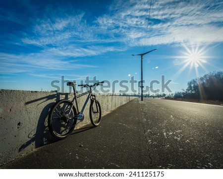Bicycle stands at the side of the road on a sunny day, empty road, sun glare, blue sky, vignette