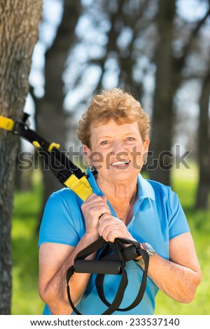 Senior woman exercising with suspension trainer in park for sport fitness
