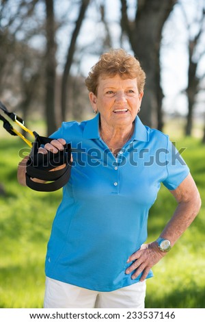 Senior woman exercising with suspension trainer in park for sport fitness