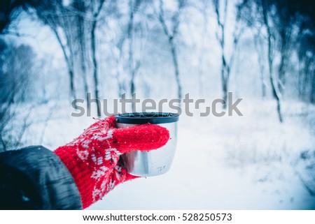 girl with long hair in red gloves with ornament holding a tourist from a thermos cup. During snowfall. Rest tourism background. Winter forest scenery blurred background. Cold winter landscape