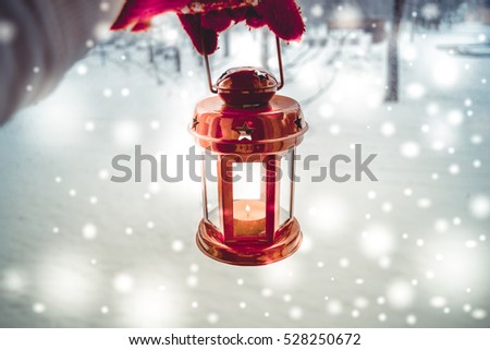 Holding in red glove a red candle lantern in the winter forest. Snow forest snowfall. Christmas Winter New Year background trembling flame Scenery. Fairy magic forest flashlight