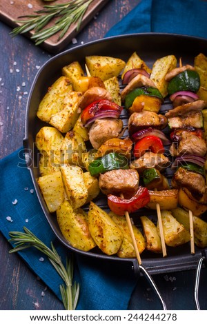 Grilled meat and vegetable kebabs and baked potatoes on pan