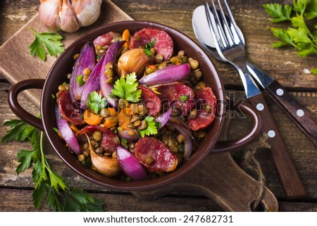 lentil with  sausage and vegetables in pot on rustic background, top view