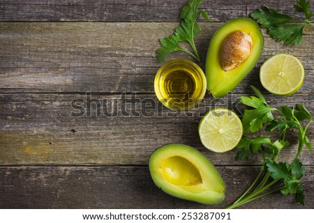 food background with fresh organic avocado, lime, parsley and olive oil on  old wooden table, top view, copy space