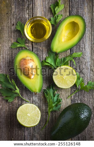 food background with fresh organic avocado, lime, parsley and olive oil on  old wooden table, top view