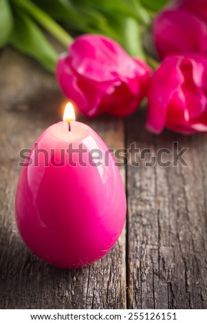 Easter candle egg and pink tulips on wooden table. Easter decoration.