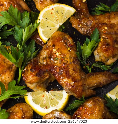Roasted chicken wings with parsley and lemon, top view, square image