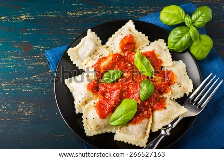 Ravioli with tomato sauce and basil on dark background, top view