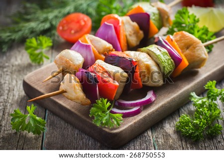 Grilled chicken and vegetable kebabs on wooden background
