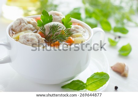 Soup with chicken meatballs and vegetables on white wooden background