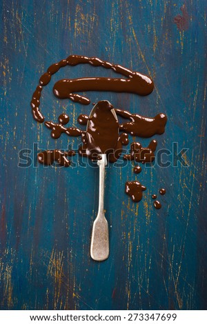 Spoon with melted chocolate on dark blue background, top view
