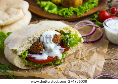 falafel with fresh vegetables in pita bread with tzatziki sauce on wooden background, selective focus