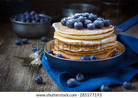 pancakes with blueberry and powdered sugar in pan on rustic background