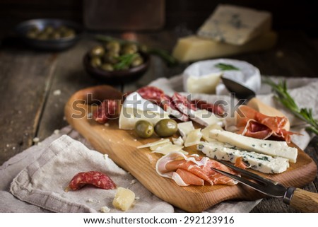 Appetizers. Various types of cheese, salami and prosciutto on  wooden cutting board, rustic background