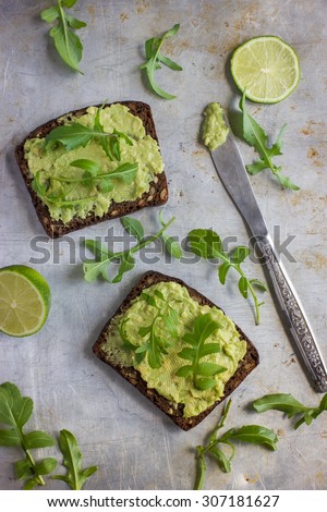 rye toasts with guacamole and arugula on rustic  background, top view
