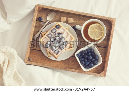 breakfast in bed,  tray with belgian waffles with blueberry and cup of lemon tea, toned, top view