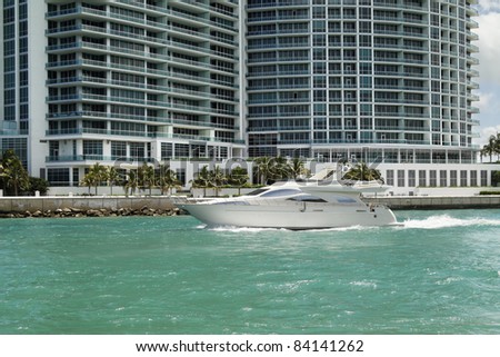Fast and expensive Luxury  pleasure yacht heading out to sea for some leisure time with some condominiums in the background