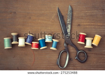 Old scissors and wooden spools of colored thread lie on a wooden table