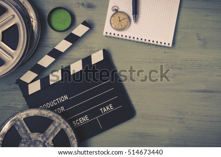 Clapperboard and a film reel, a stop watch, a notebook and a lens on the table