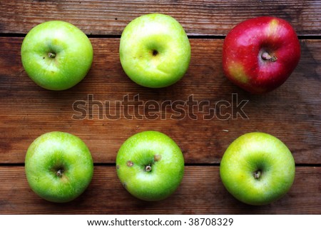 One red and five green apples on wooden surface.
