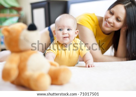 young Mother and baby lying on the bed playing with a bear toy