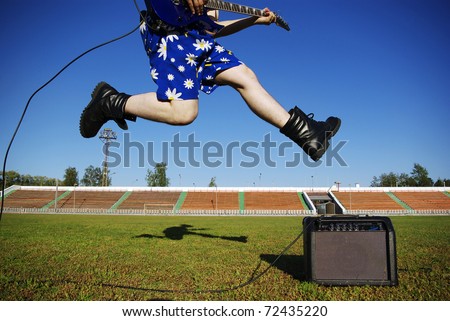 young man jumps with guitar on grass
