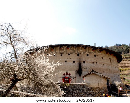 The Earth Tower of Hakka  -an ancient Chinese building in Hujian, China which was in the list ofthe  world heritage by UNESCO. In front of the building, a plum blossom tree abloom in spring.