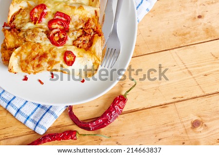 Top close up view showing enchiladas dish with chili peppers on a wooden table