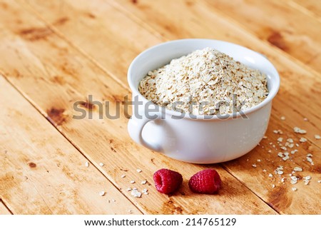 Raw oatmeal in a bowl with raspberries, on a wooden table, wide angle
