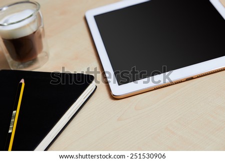 Hands holding digital tablet on a wooden desk with coffee and organiser