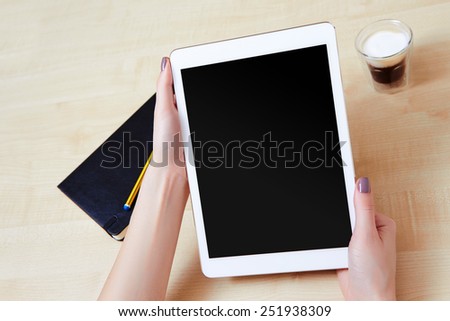 Woman holding a white digital tablet in portrait mode over a wooden desk with a coffee and organiser